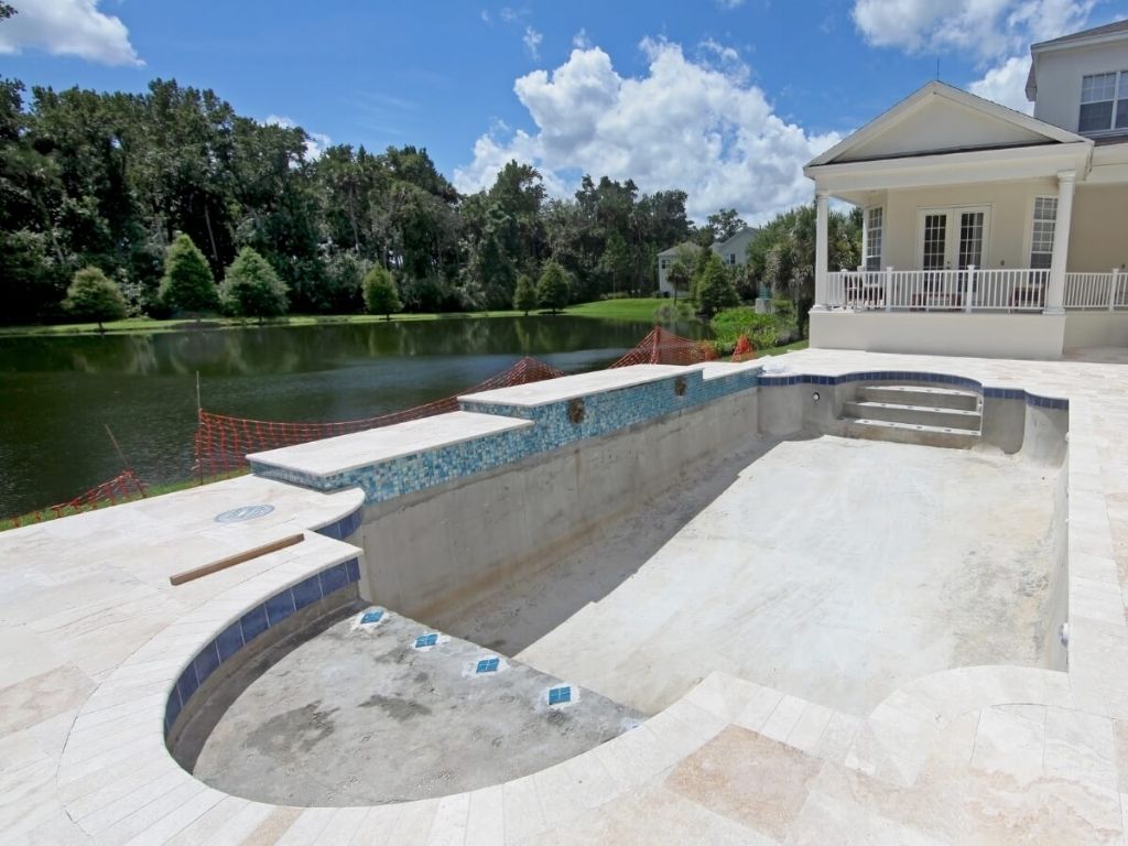 A pool under construction by SiteWorx Pools in Odessa, showing the progress with partially finished tiles and steps, overlooking a beautiful natural lake in the background.